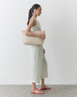 Person in a sleeveless jumpsuit holding a shoulder bag, wearing sandals.