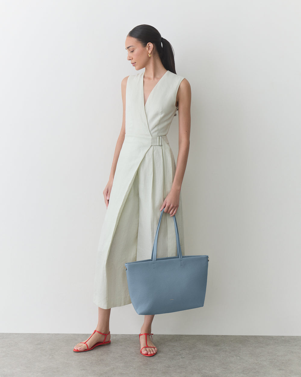Person in sleeveless dress holds large handbag, stands in a relaxed pose.