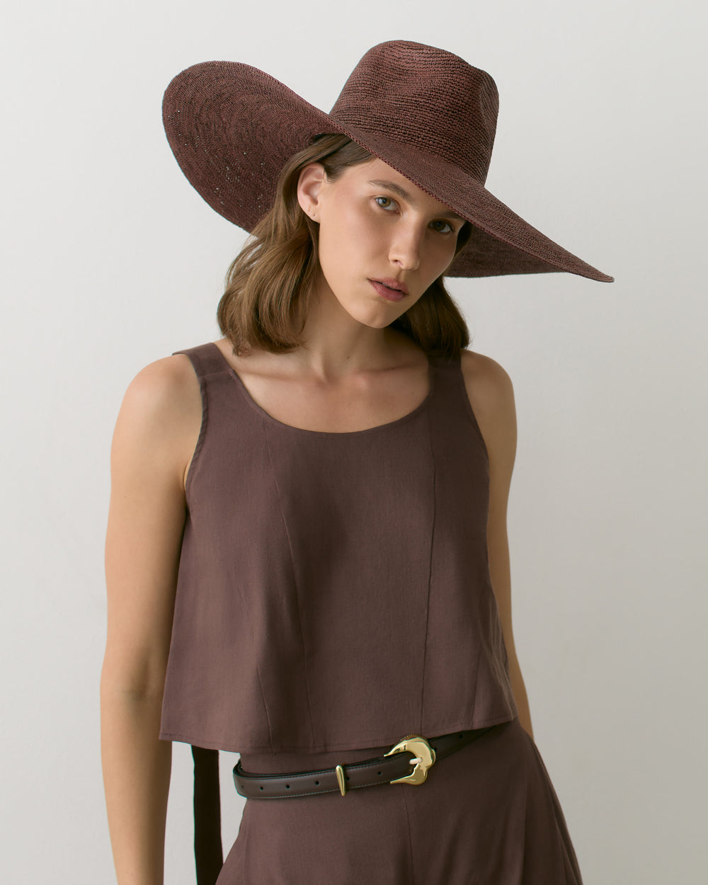 Woman wearing sleeveless top with wide-brimmed hat.