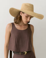 Woman in sleeveless top and wide-brimmed hat looking down.