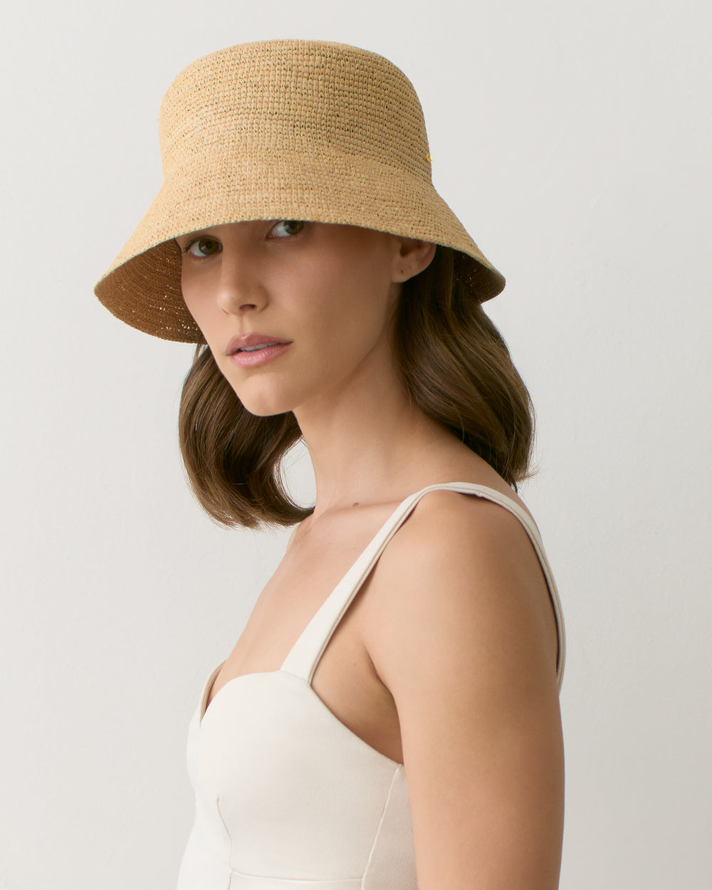 Person wearing a straw hat and a sleeveless top looking at the camera.