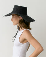 Woman in sleeveless top wearing wide-brimmed hat with a chin strap.
