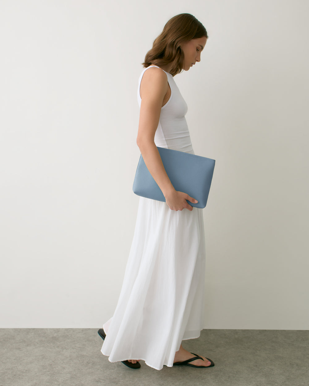 Person in sleeveless dress holding a large clutch bag, walking to the right