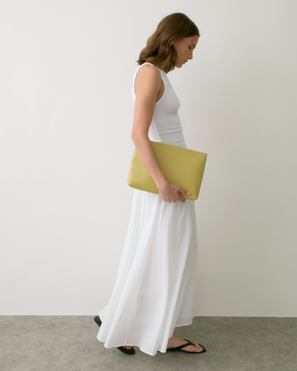 Person in long dress holding a rectangular clutch while walking indoors.