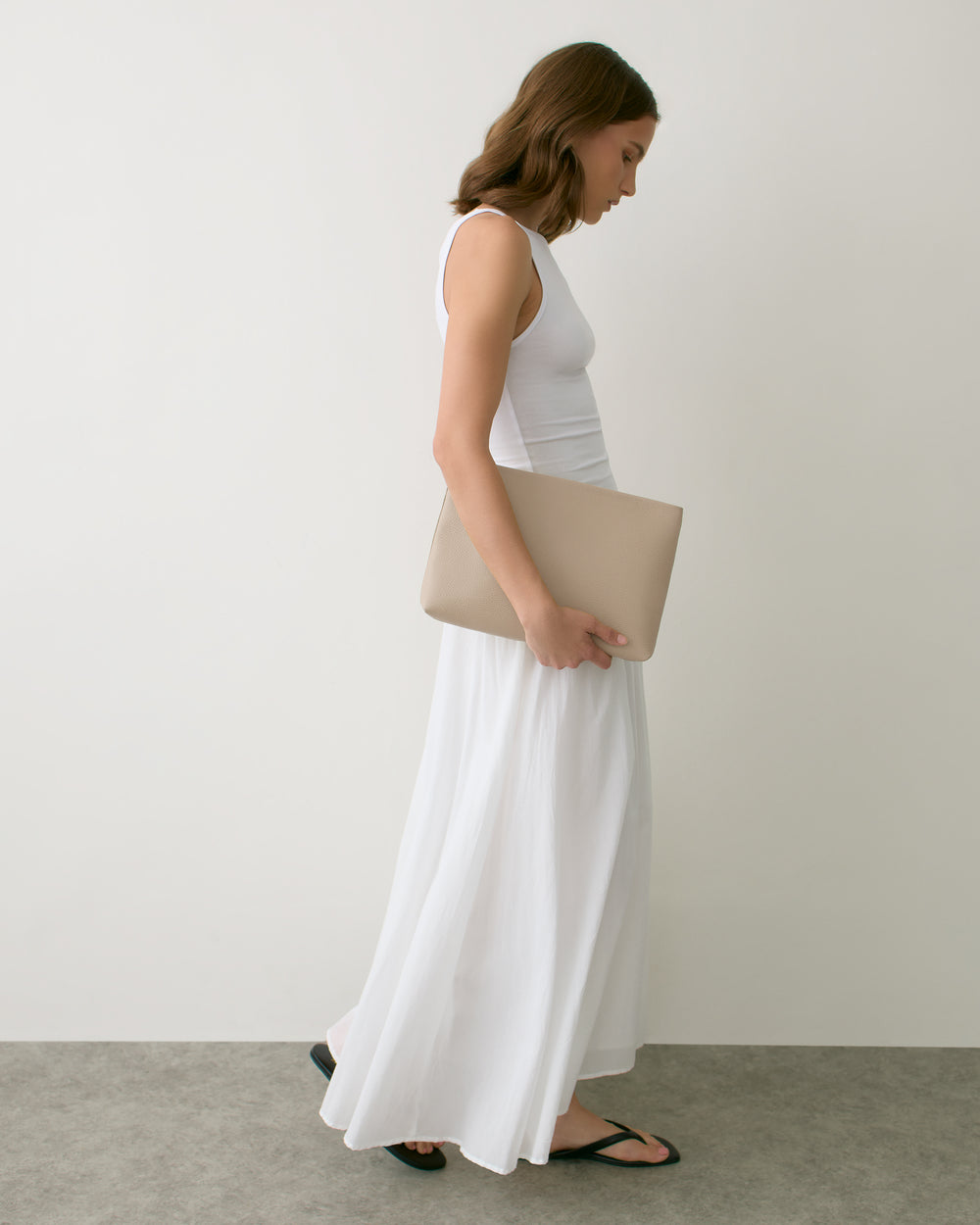 Person in long dress holding large clutch bag, wearing sandals, walking indoors.