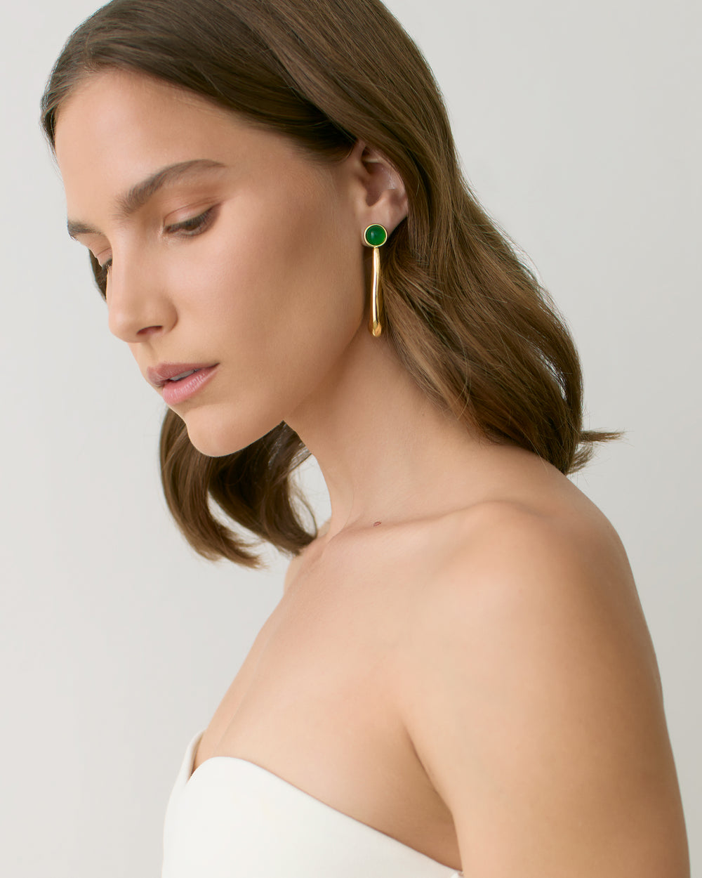Person wearing drop earrings with bare shoulders, looking down.