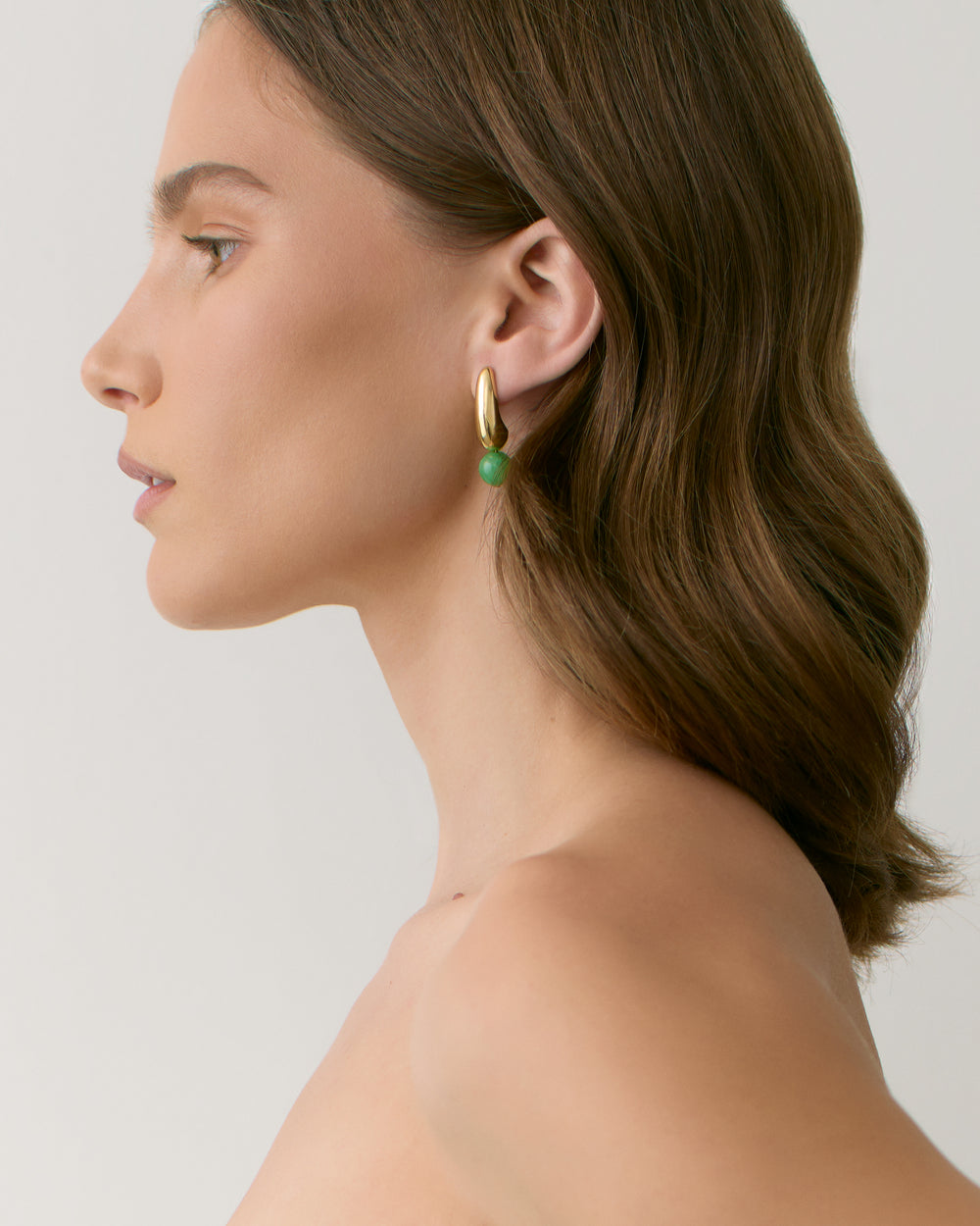 Person wearing a hoop earring with a green bead, shown in profile.