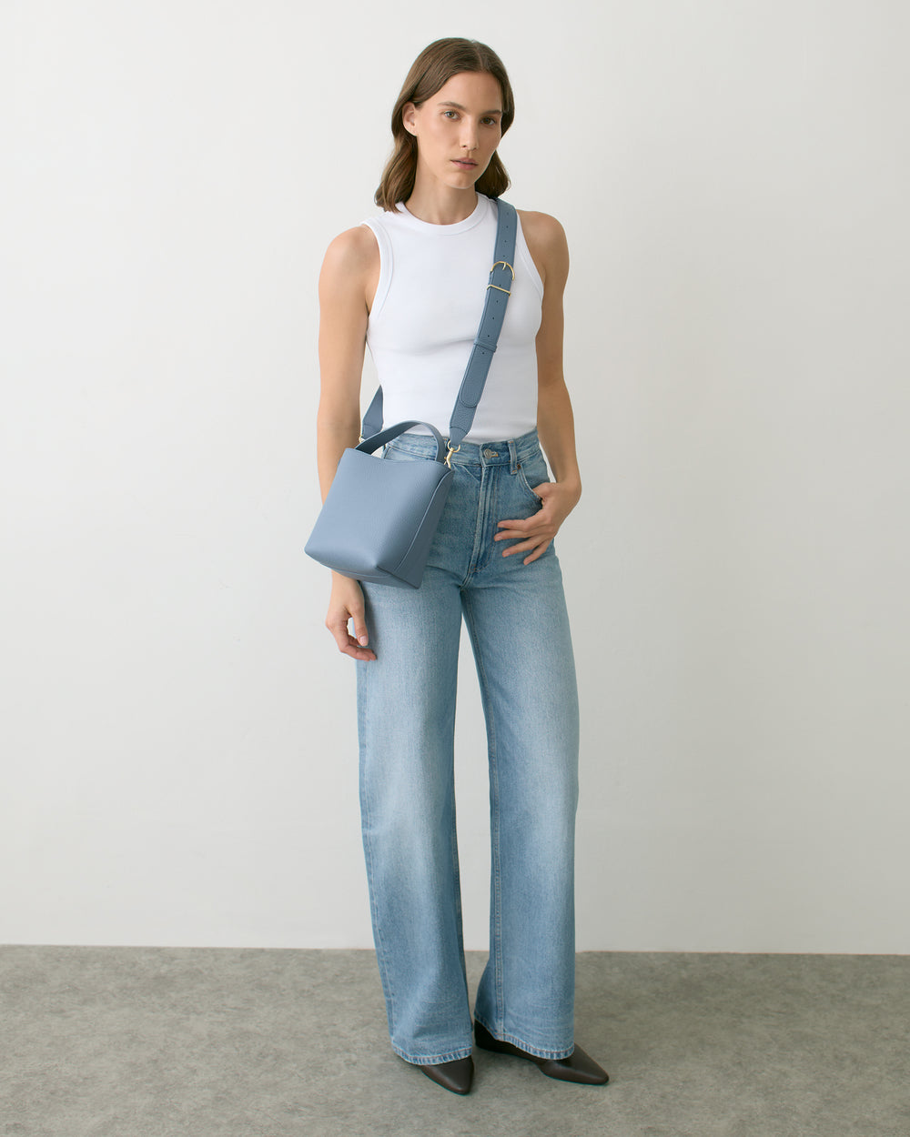 Person wearing a sleeveless top, jeans, holding a square bag with a strap across the chest.