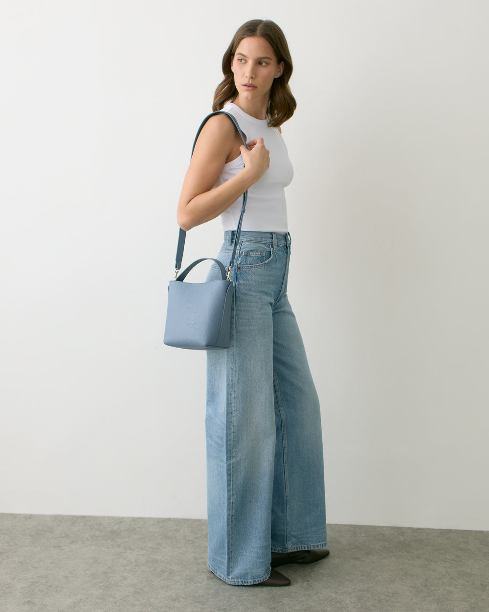 Person standing with shoulder bag, wearing wide-leg jeans and sleeveless top.