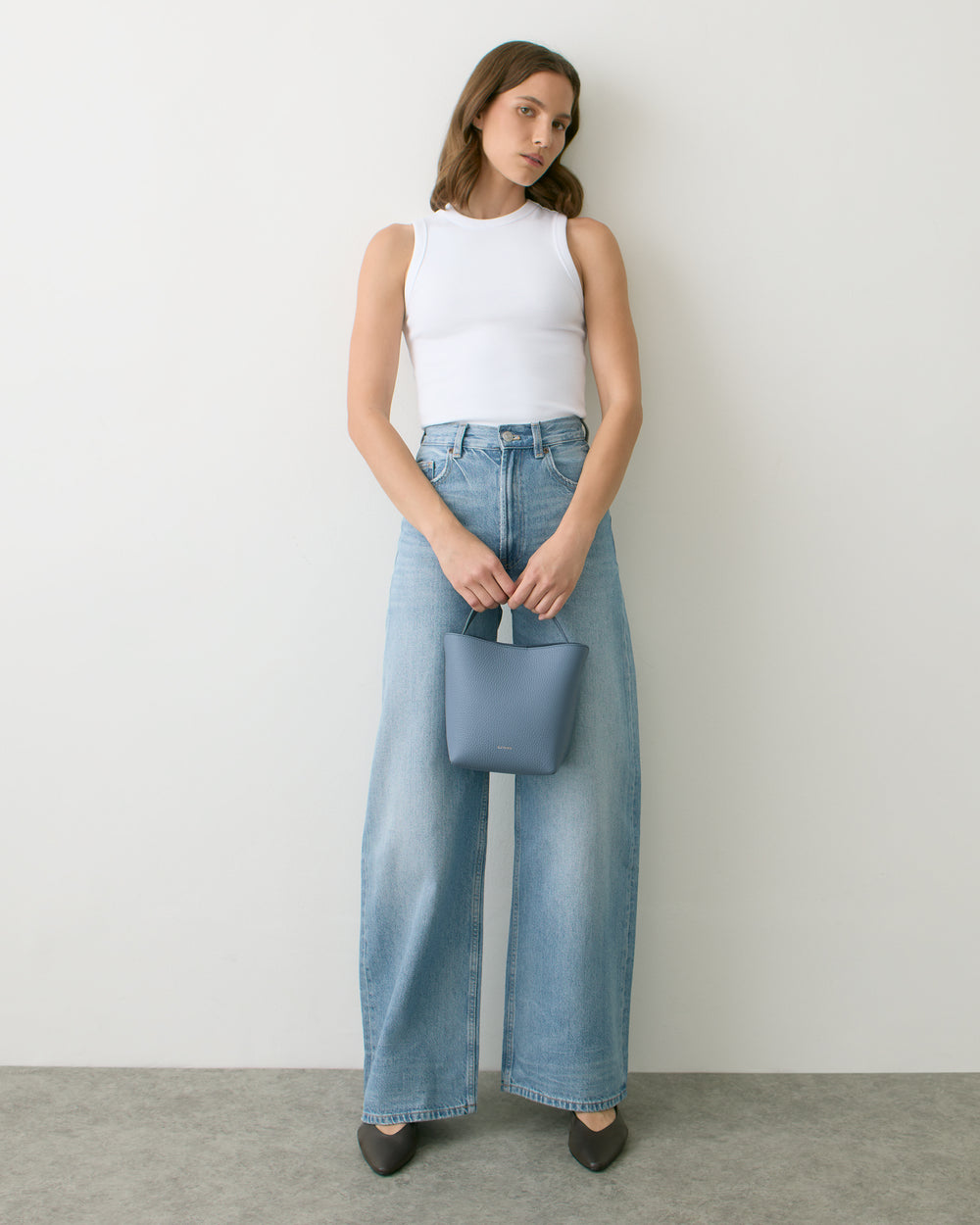 Person in sleeveless top and wide jeans holding small handbag.