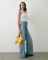 Person in a sleeveless top and wide-leg jeans holding a handbag with scarf detailing.