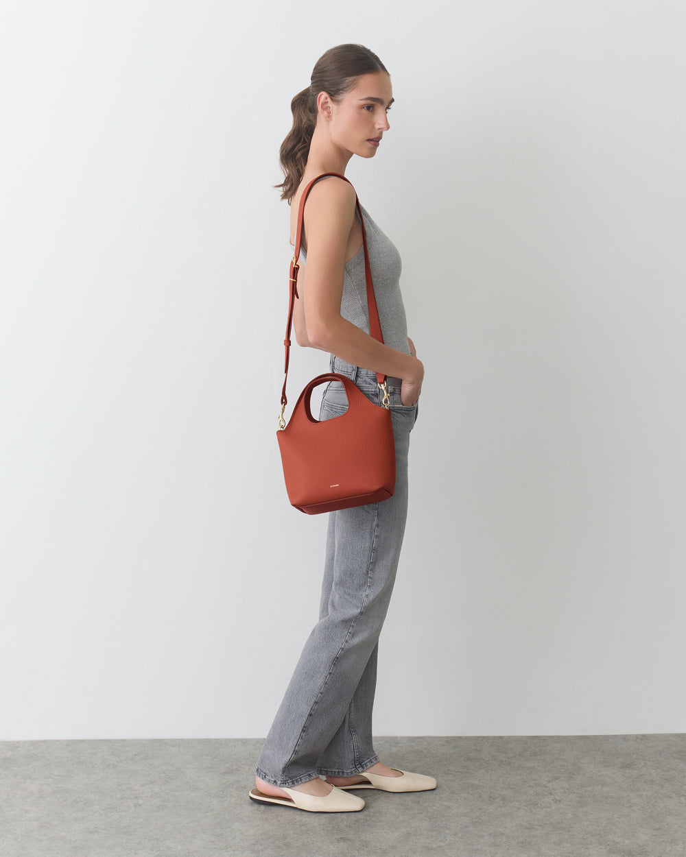 Person standing, wearing a sleeveless top, jeans, flats, holding shoulder bag.
