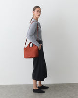 Person standing with a shoulder bag, wearing a long skirt and long-sleeved top.