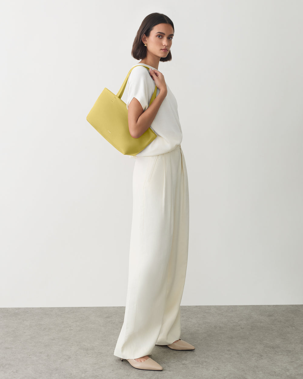 Person posing with a shoulder bag, wearing a sleeveless shirt and wide-leg trousers.