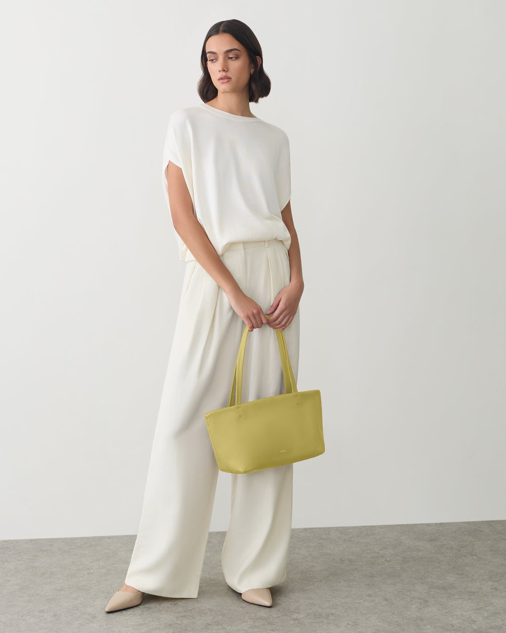 Person standing in wide-leg pants holding a tote bag
