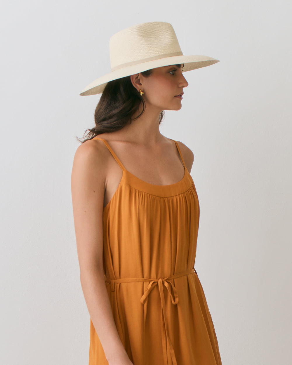 Woman in a sleeveless dress and wide-brim hat looking to the side.
