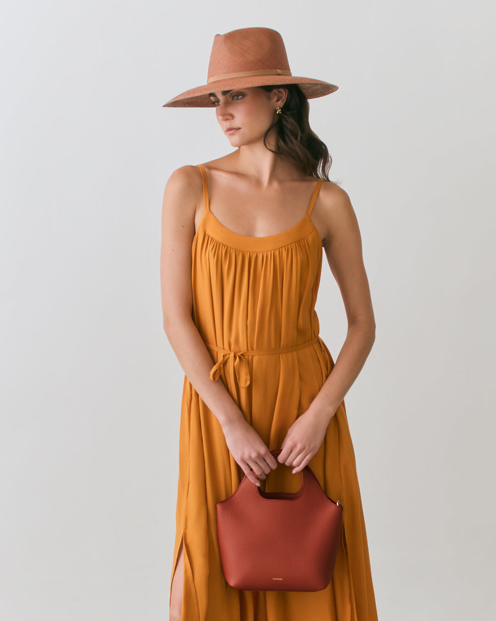 Person in dress and hat holding a handbag.
