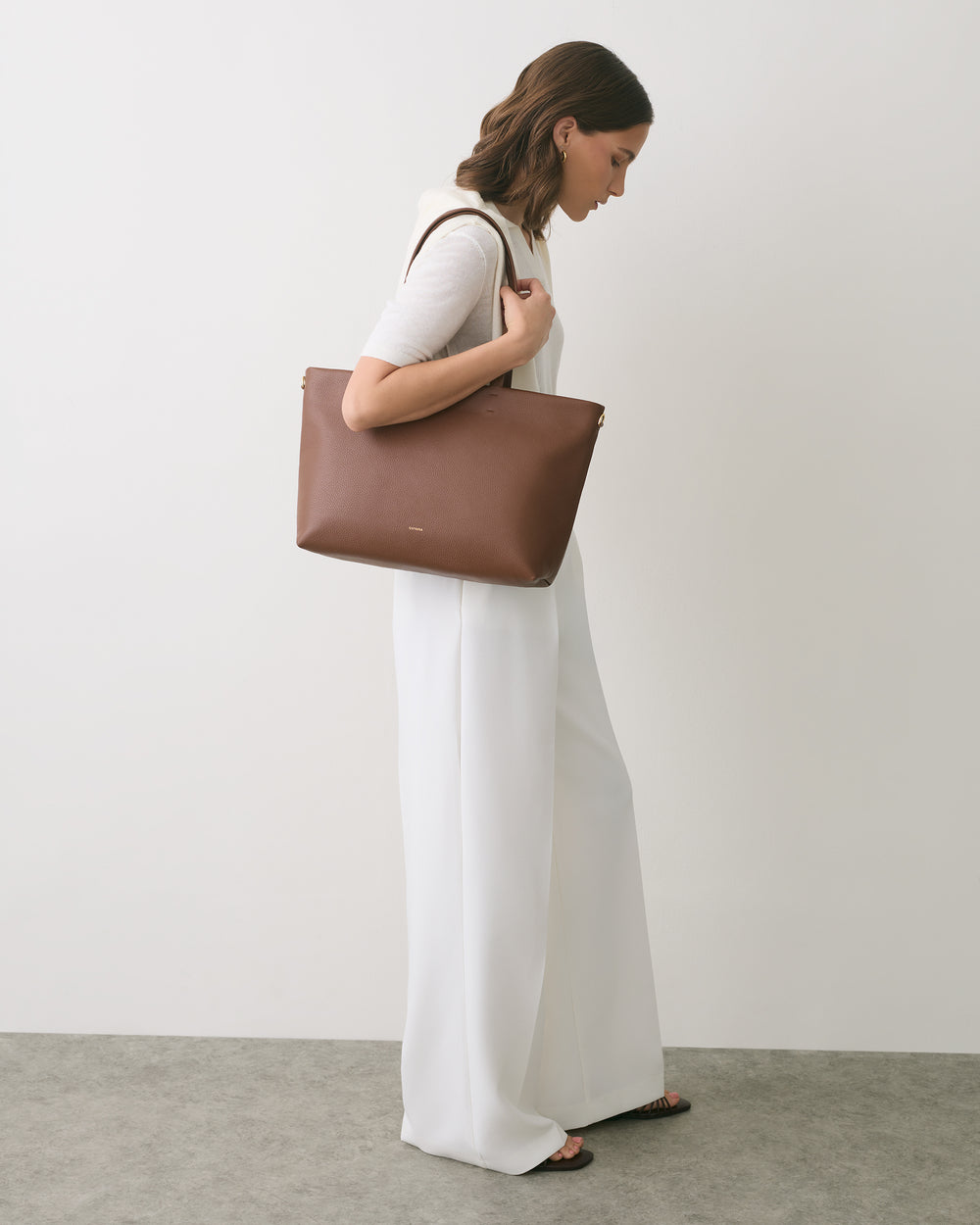 Person in white outfit holding a large handbag over shoulder.