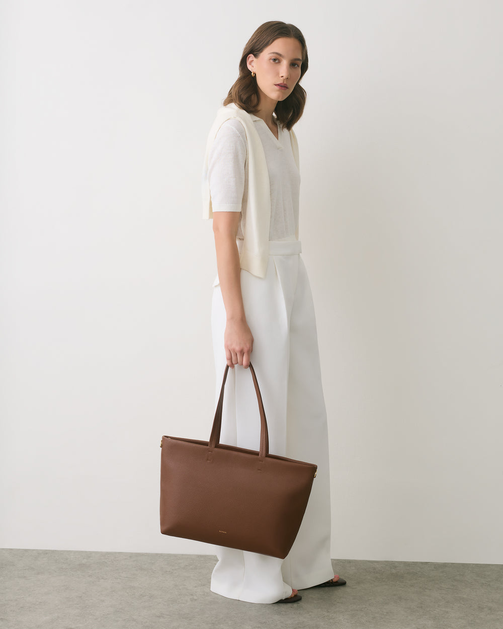 Person standing with a large handbag in a minimalist setting.
