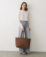 Person in sweater and jeans holding a large tote bag