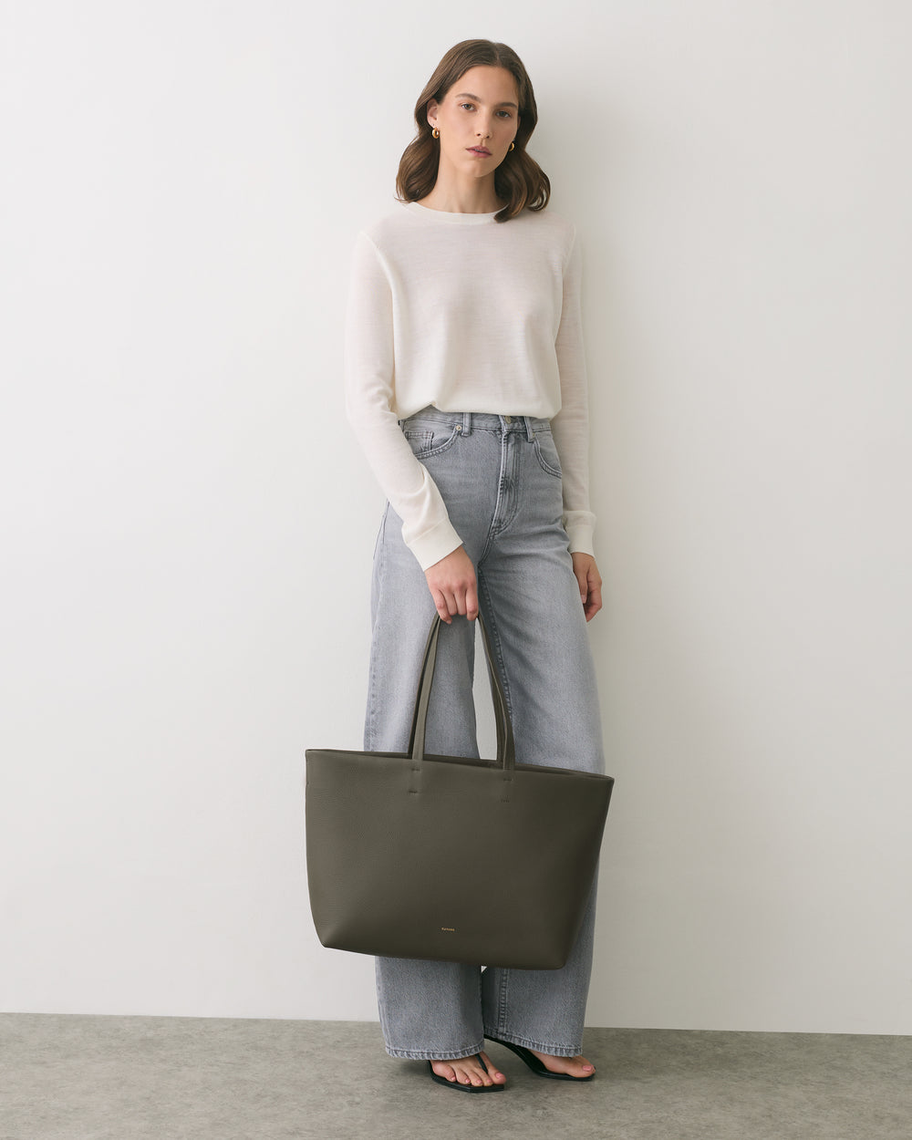 Person in casual outfit holding a large tote bag, standing against a plain background.