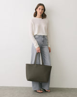 Person in casual outfit holding a large tote bag, standing against a plain background.