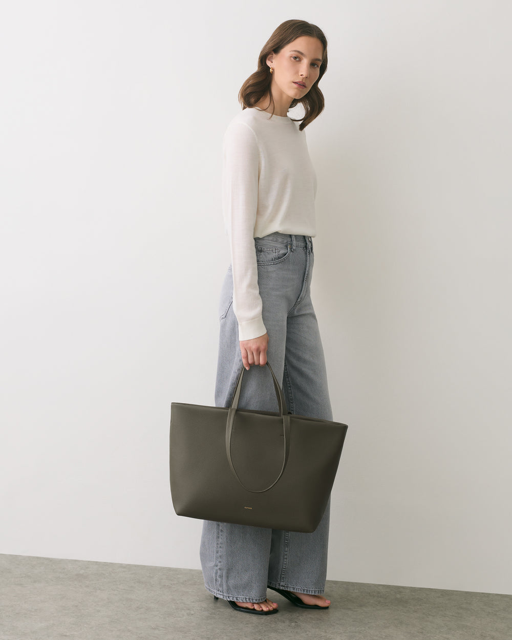 Person holding large tote bag, standing against a plain background.