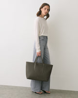 Person holding large tote bag, standing against a plain background.