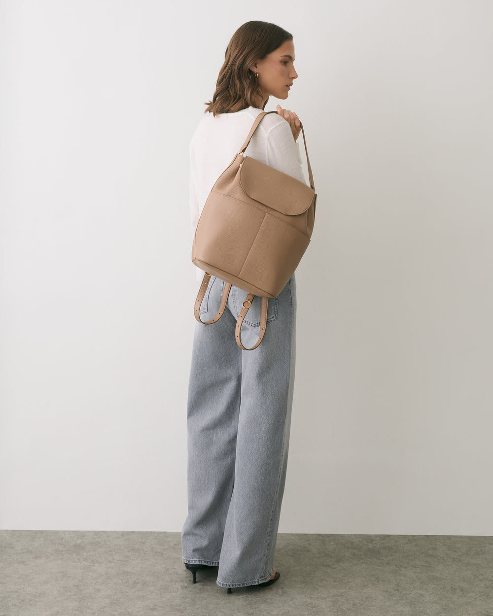 Person wearing a sweater and wide-leg jeans, holding a backpack over one shoulder.