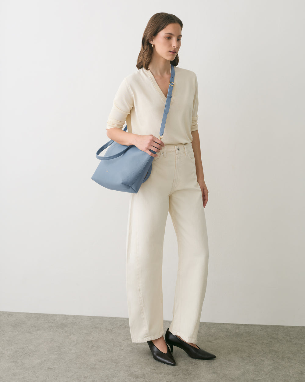 Person wearing light outfit with shoulder bag, standing on a plain background.
