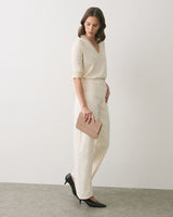 Woman in casual outfit holds a clutch, standing on a plain background.