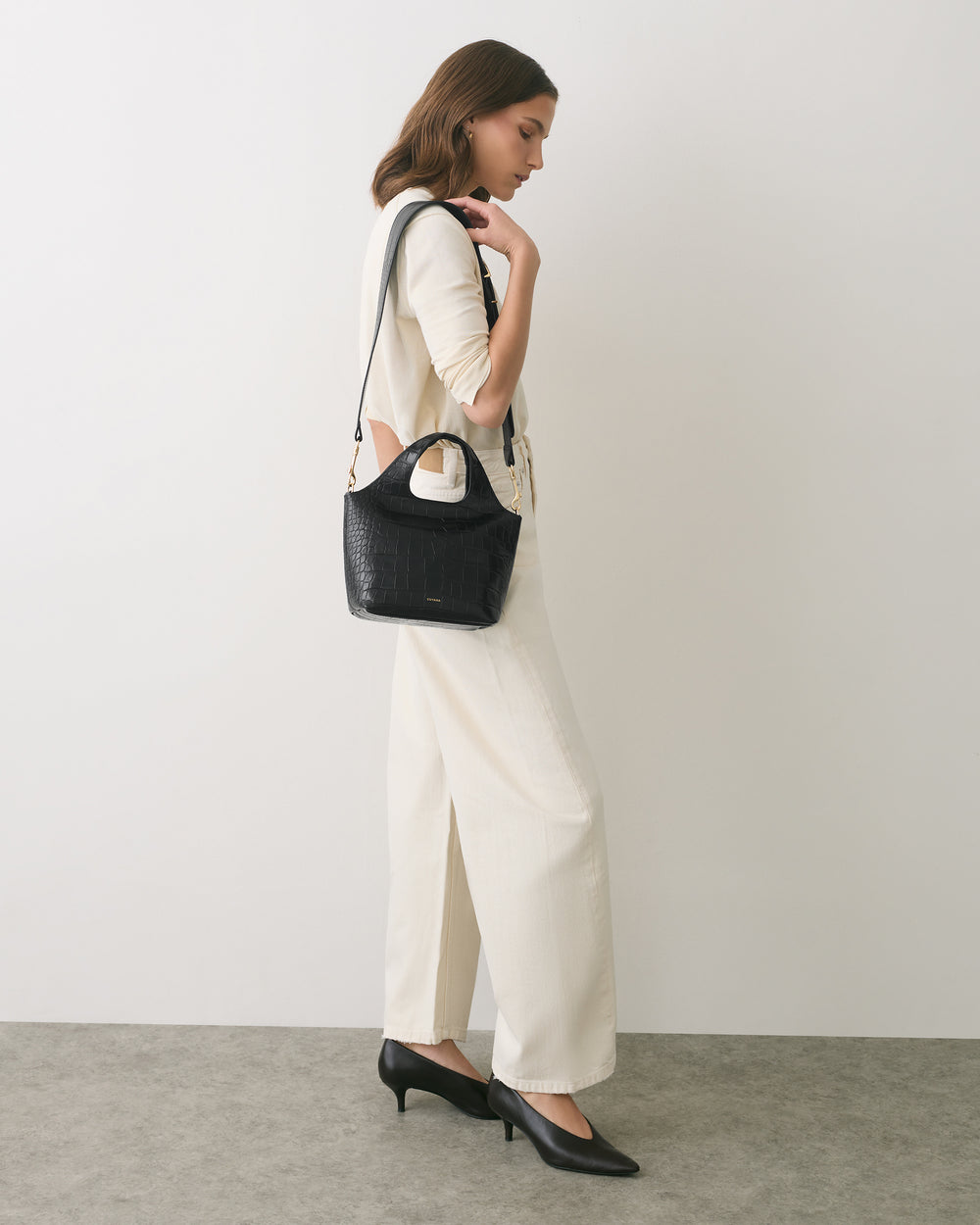 Person in profile with croc-embossed bag, wearing long pants and heeled shoes.