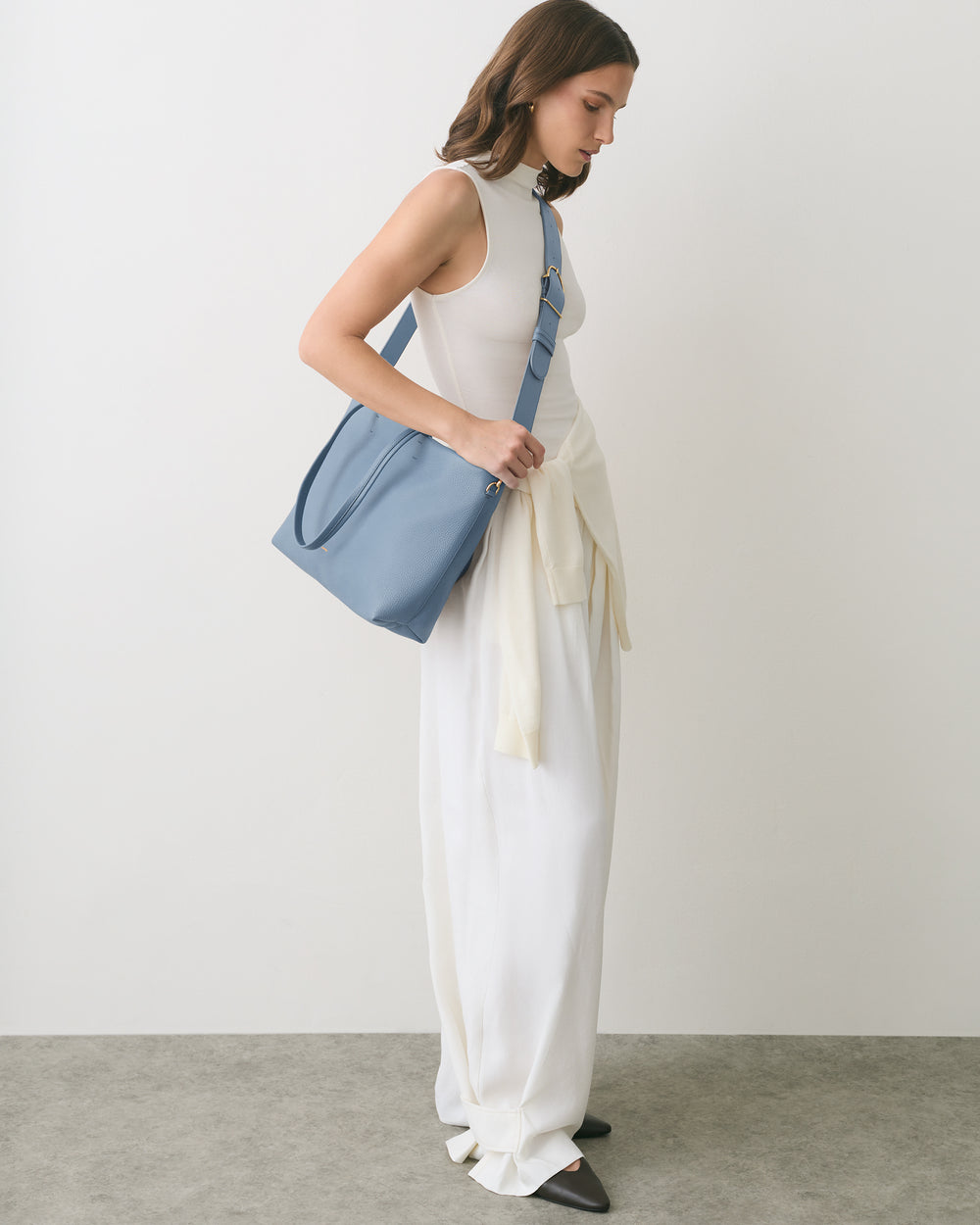 Person wearing a long dress with a bag over shoulder, sweater tied at waist.