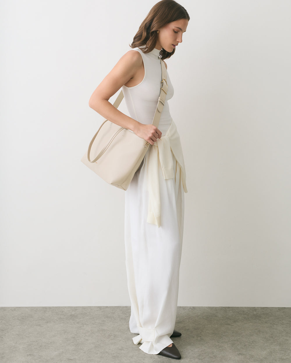 Person in a sleeveless dress with a sweater tied at the waist and a shoulder bag.