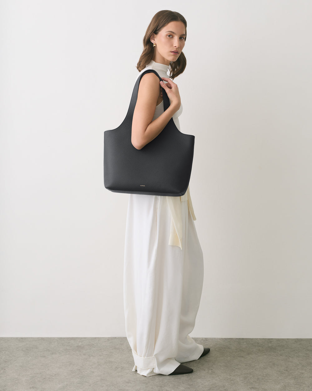 Person holding a large tote bag, wearing a long, flowing outfit.