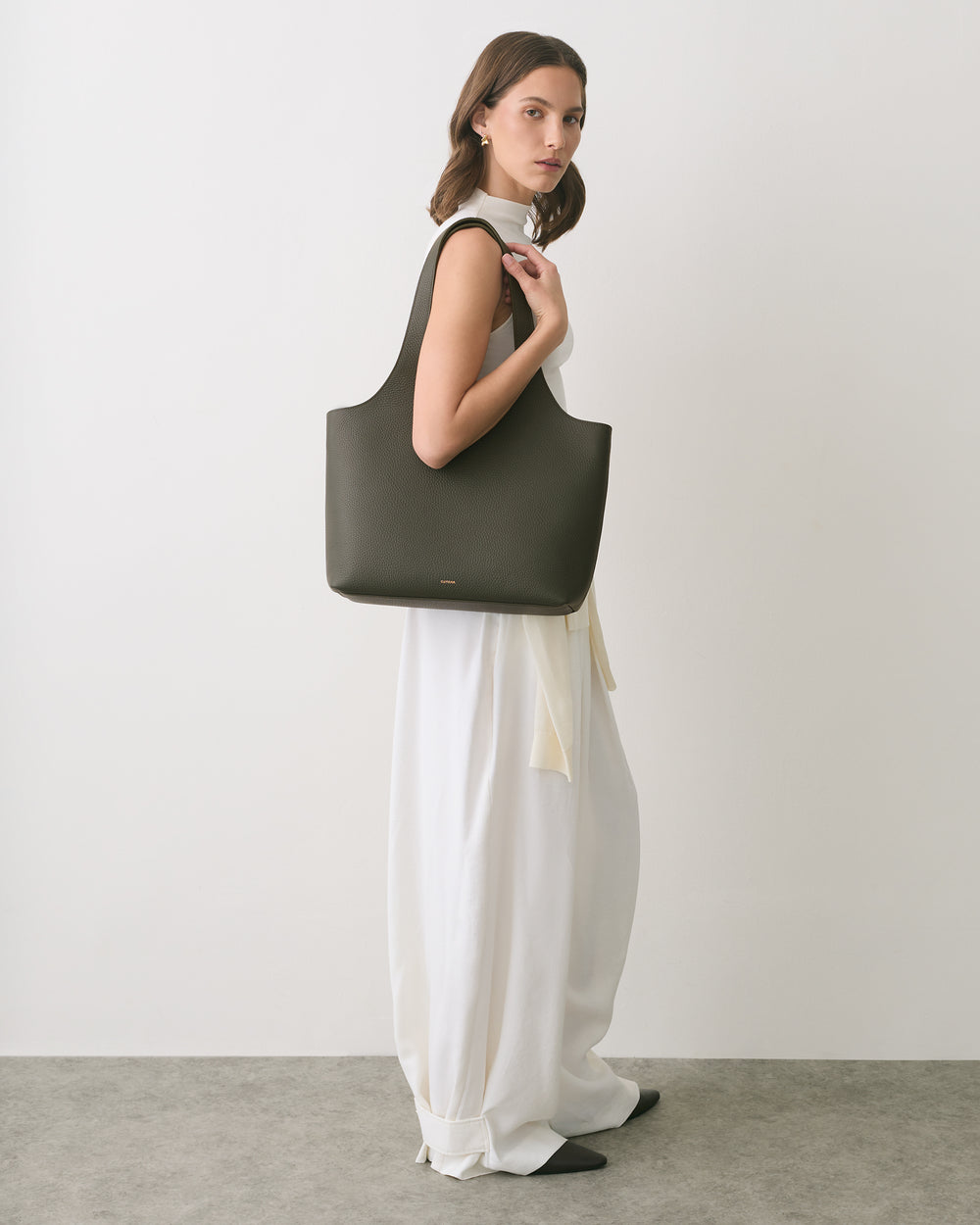 Person in dress holding large handbag while looking sideways.