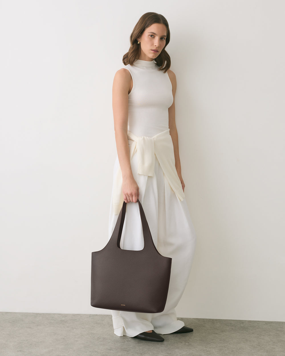 Woman in sleeveless top and wide pants holds a handbag.