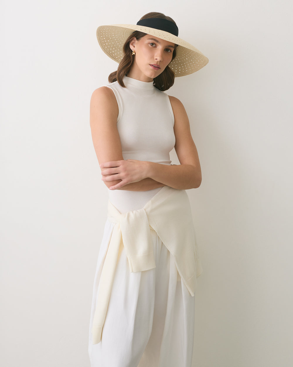 Person wearing a sleeveless top, wide-brim hat, and skirt, with a sweater tied around waist.