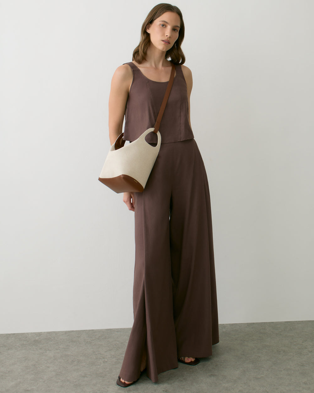 Person in sleeveless top and wide-leg pants holding a handbag.