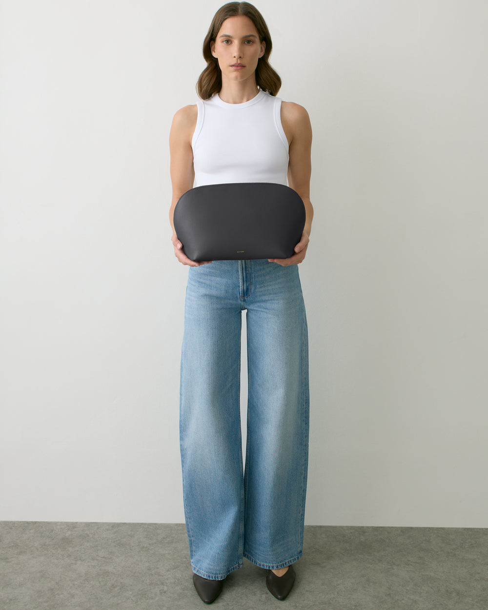 Person holding a large oval clutch, wearing a sleeveless top and wide-leg jeans.