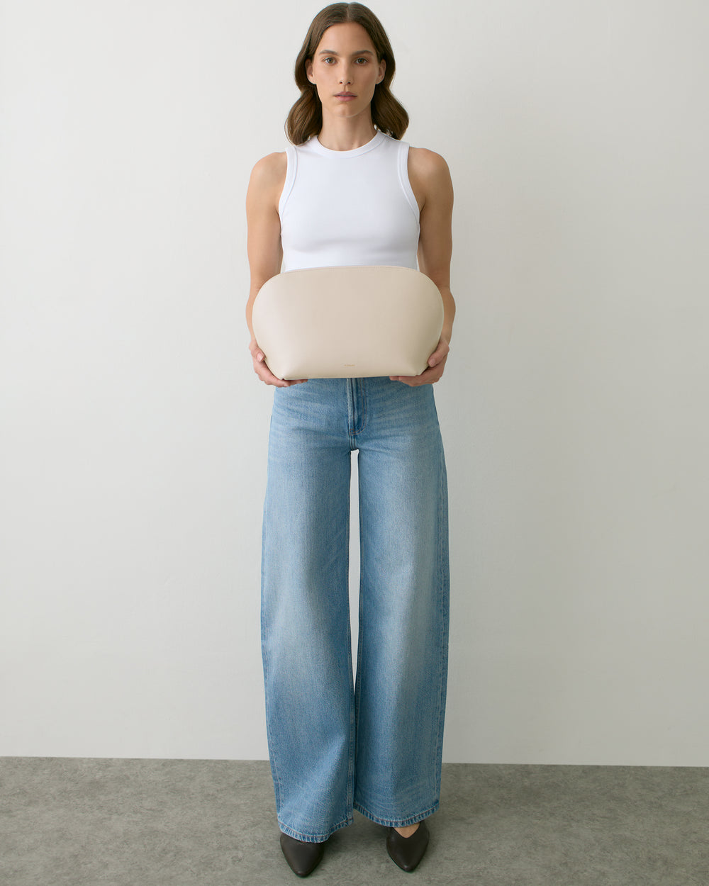 Person holding a rounded bag, wearing a tank top and wide-leg jeans.