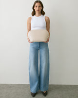 Person holding a rounded bag, wearing a tank top and wide-leg jeans.