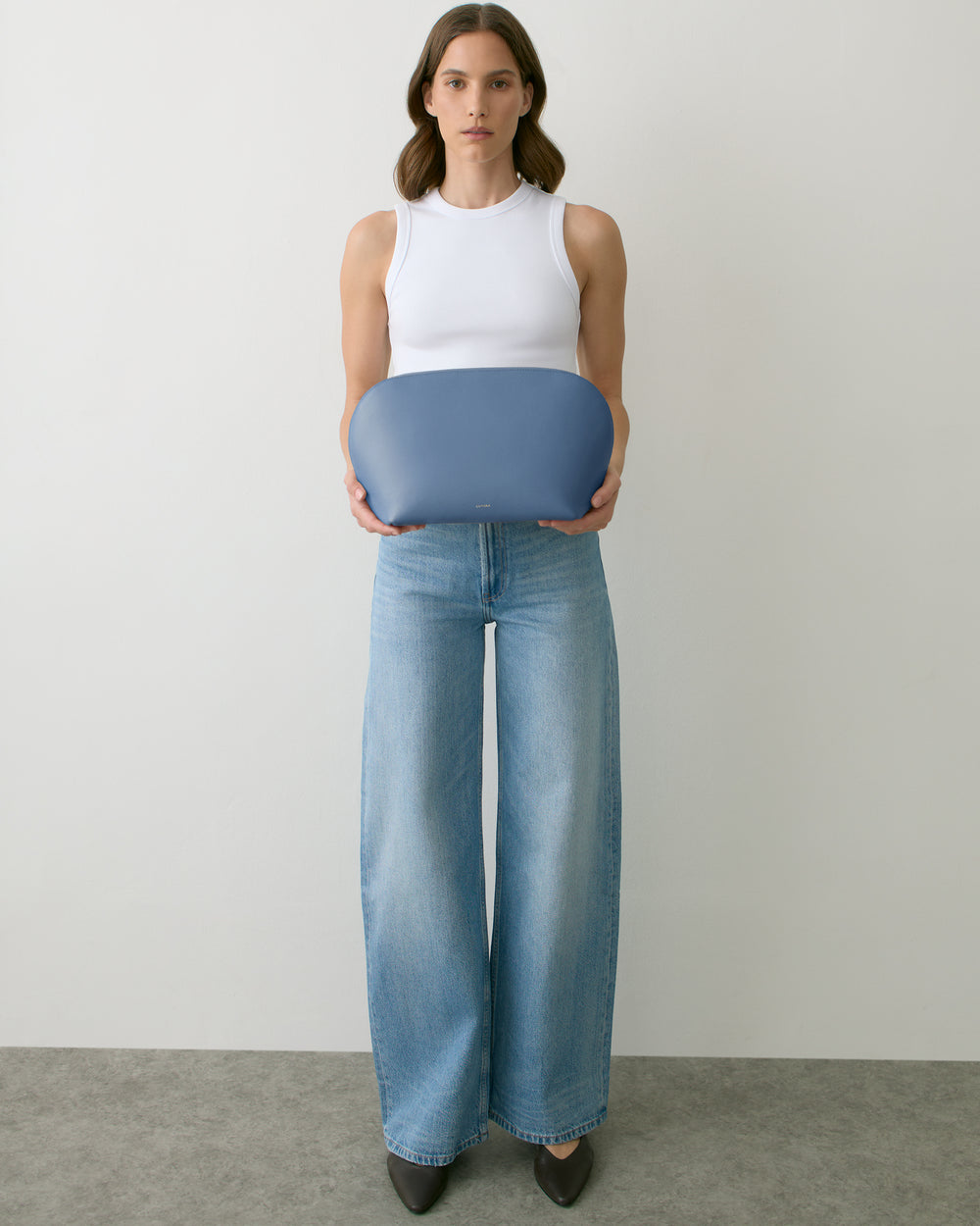 Person holding a large, rounded clutch bag wearing a sleeveless top and wide-leg jeans.