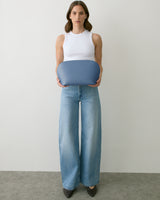 Person holding a large, rounded clutch bag wearing a sleeveless top and wide-leg jeans.