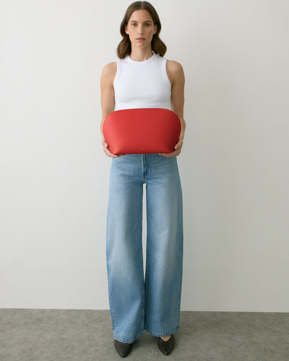 Person holding a round bag, wearing a sleeveless top and wide-leg jeans.