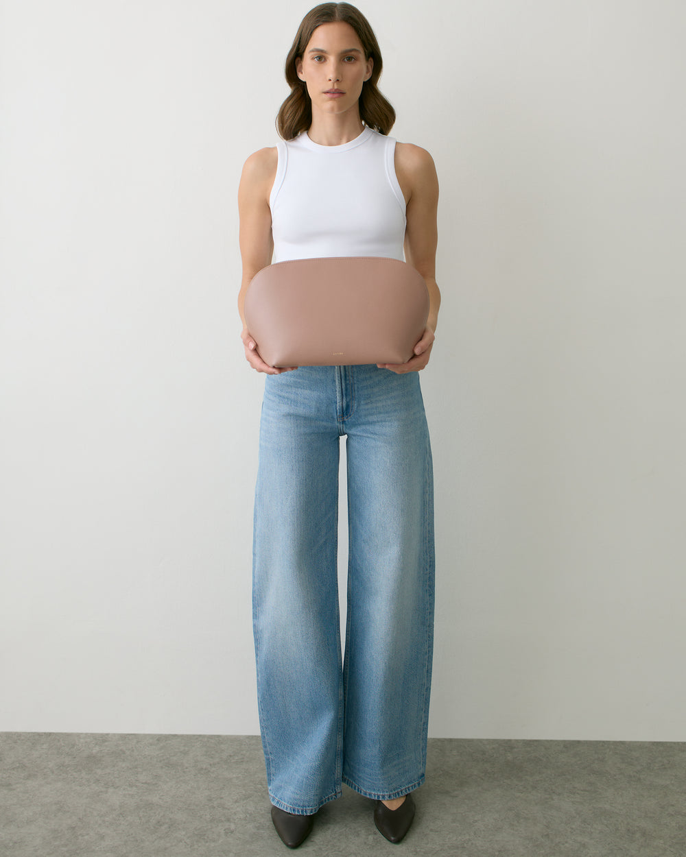 Person holding a round bag, wearing a sleeveless top and wide-leg jeans.