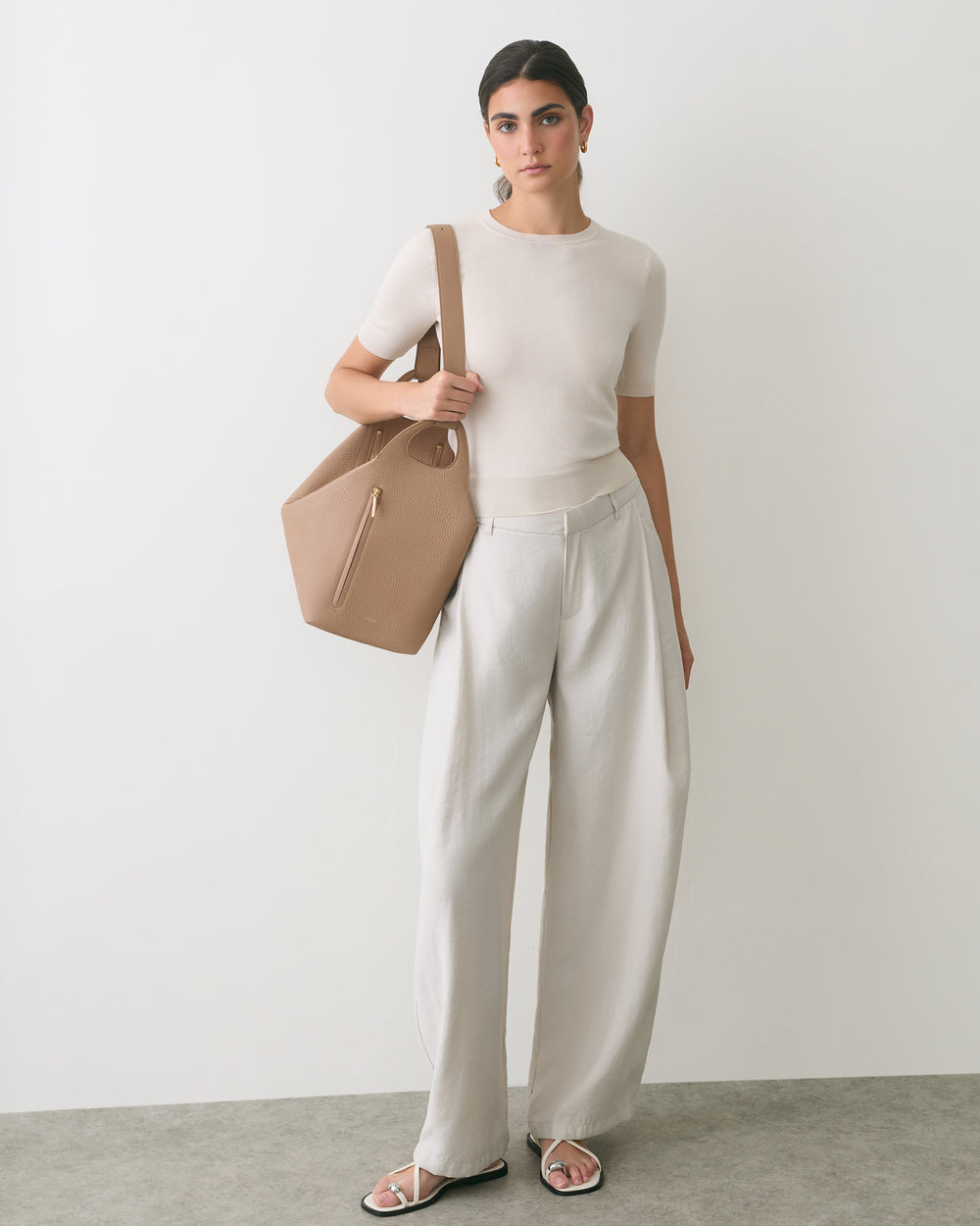 Person in a t-shirt and wide pants holds a large handbag, wearing sandals.