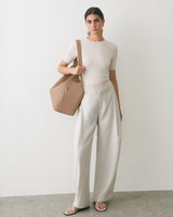 Person in a t-shirt and wide pants holds a large handbag, wearing sandals.