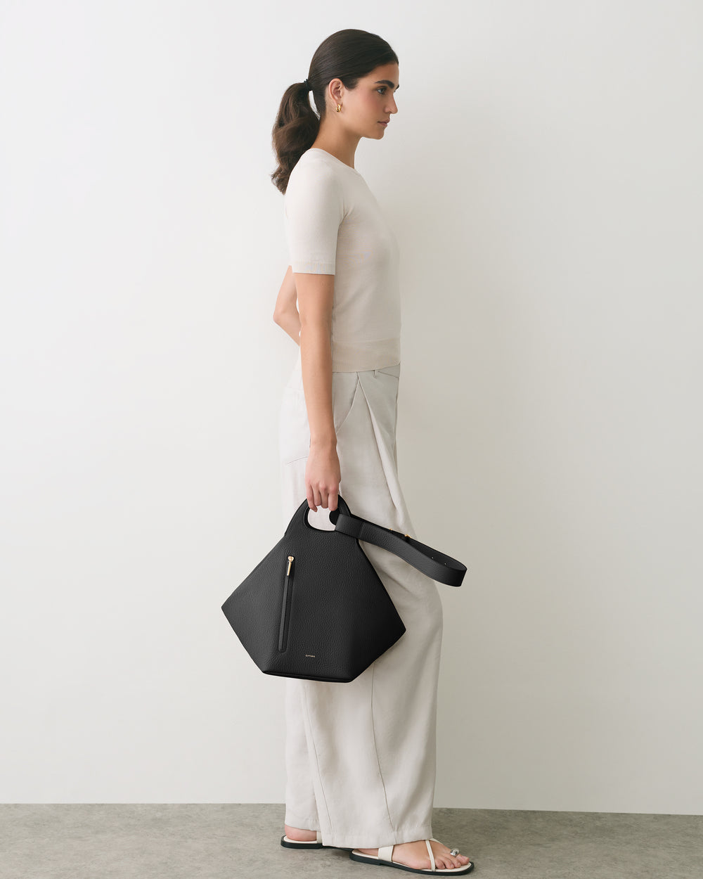 Person standing with a geometric handbag wearing a short sleeve top and loose pants.