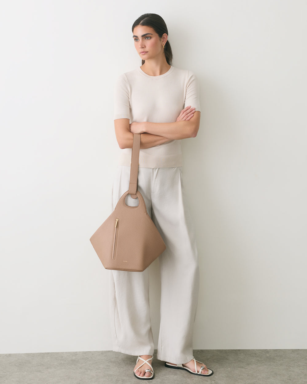 Person leaning on wall holding a geometric handbag, wearing a short-sleeve shirt and wide-leg pants.
